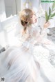 A woman in a white dress sitting on a bed holding a flower.