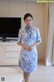 A woman in a blue and white cheongsam standing in front of a television.