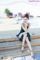 A woman in a green dress sitting on a wooden deck next to a pool.