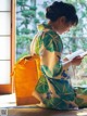 A woman in a kimono sitting on the floor reading a book.