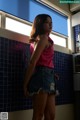 A woman in a pink top and denim skirt standing in a kitchen.