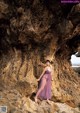 A woman in a purple dress standing on a rocky beach.