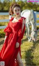 A woman in a red dress standing next to a white horse.