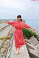 A woman in a red dress standing on a concrete wall.